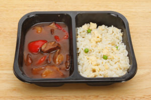 Oriental microwave meal, duck in plum sauce with egg fried rice in a plastic carton on a wooden board